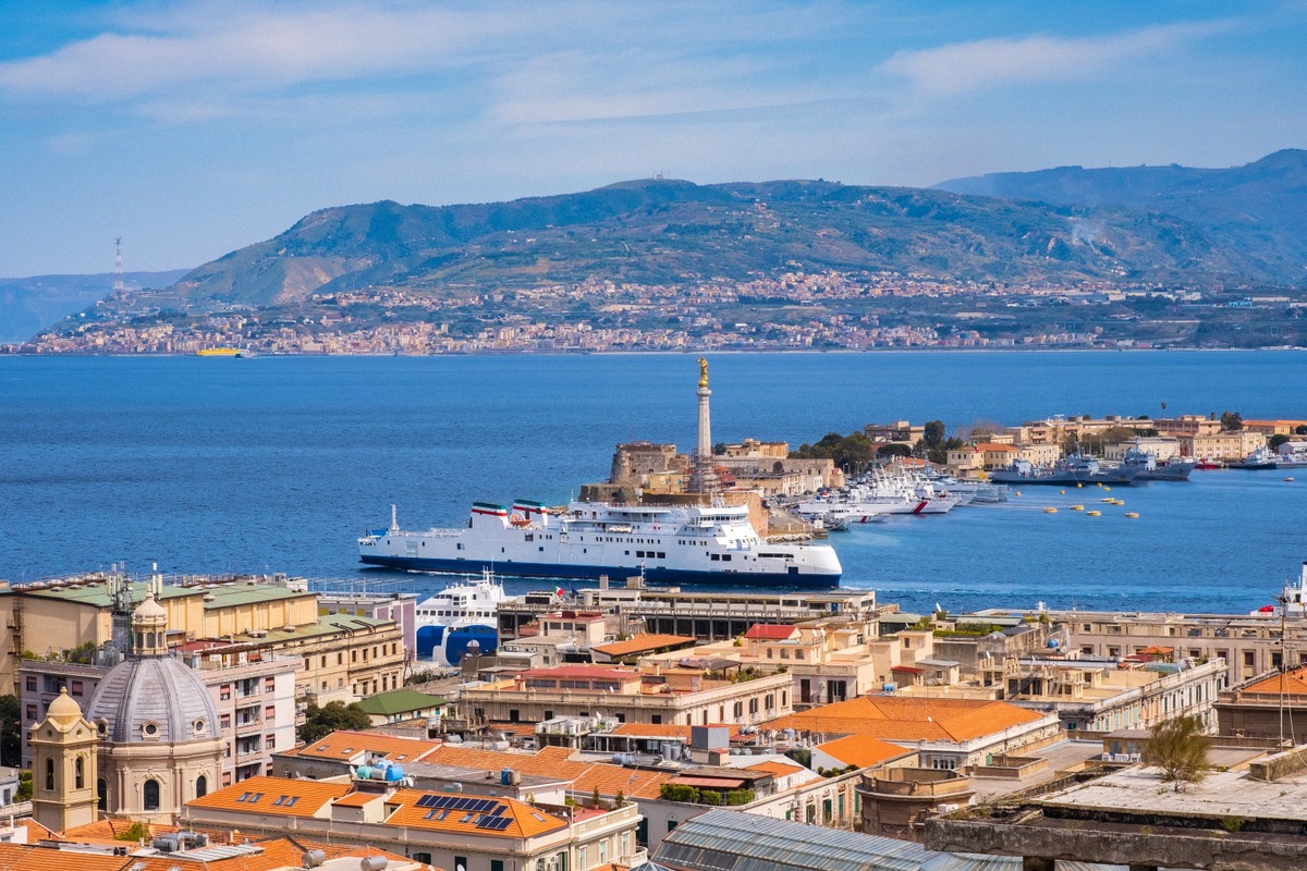 Vista del puerto de Mesina con la estatua de la Madonna della Lettera, un ferry en el terminal y la costa calabresa al otro lado del estrecho